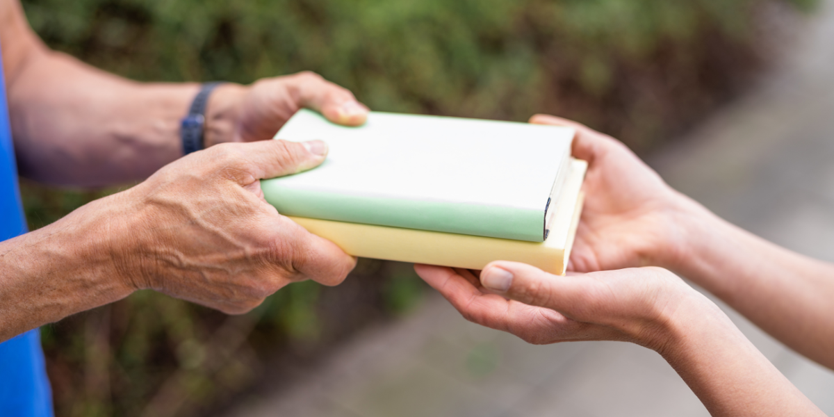 Person handing books to another person.