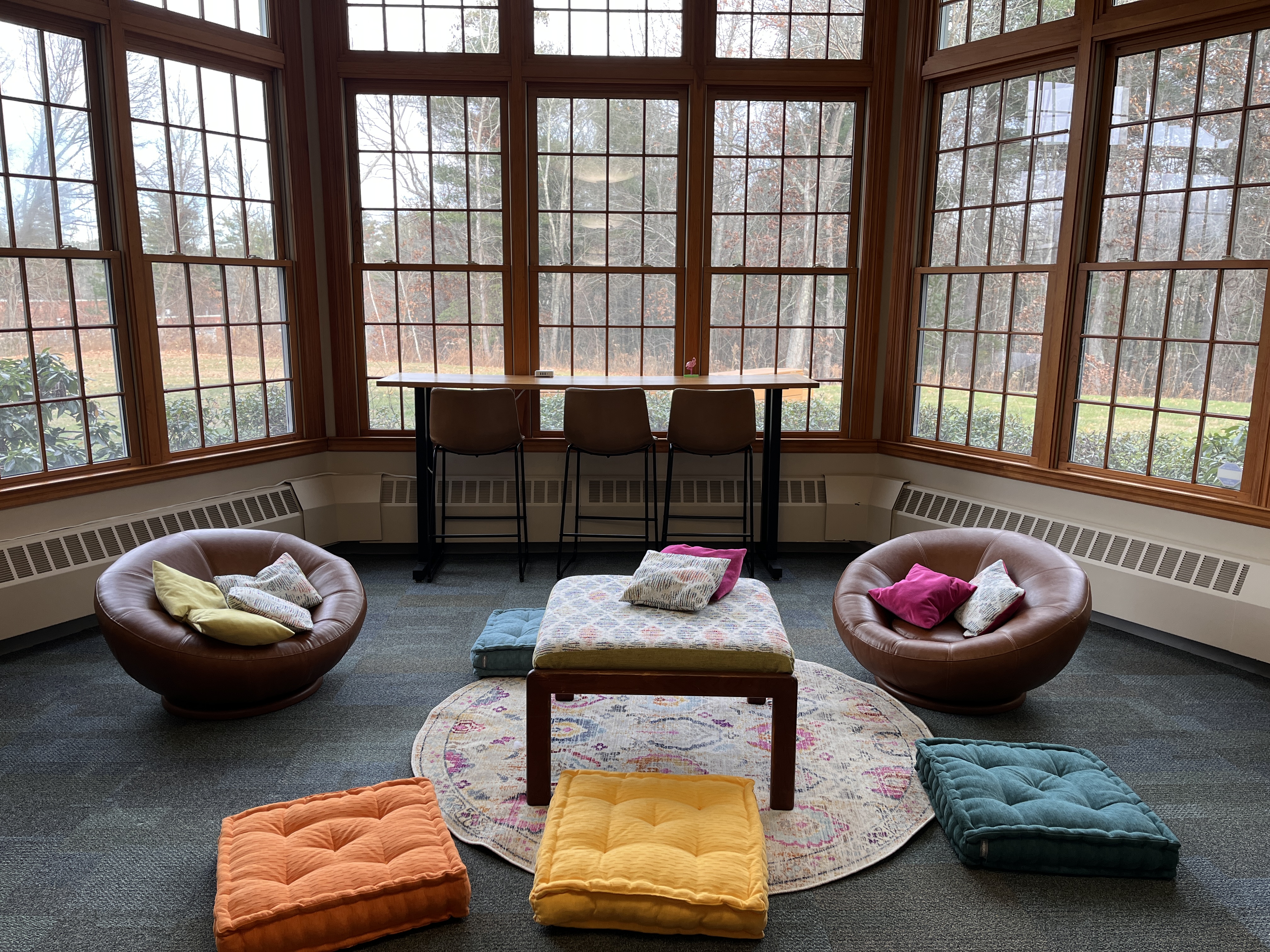 The upgraded Teen Space at Nesmith Library, including new chairs, several pillows, and a bar style table that looks out on the Library lawn with barstool style chairs. 