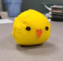 Photo of softie chick figure, yellow, resting on a desk surface
